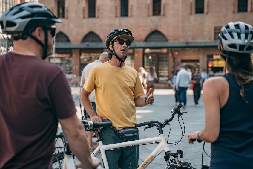A person on a bicycle in an urban setting with buildings and pedestrians in the background. 2