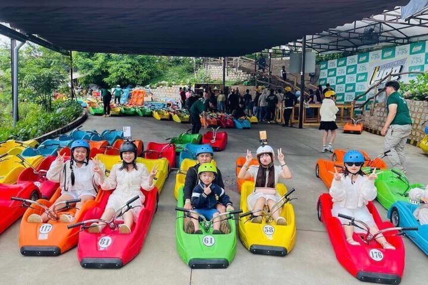 People in colorful go-karts lined up on a paved area. 1