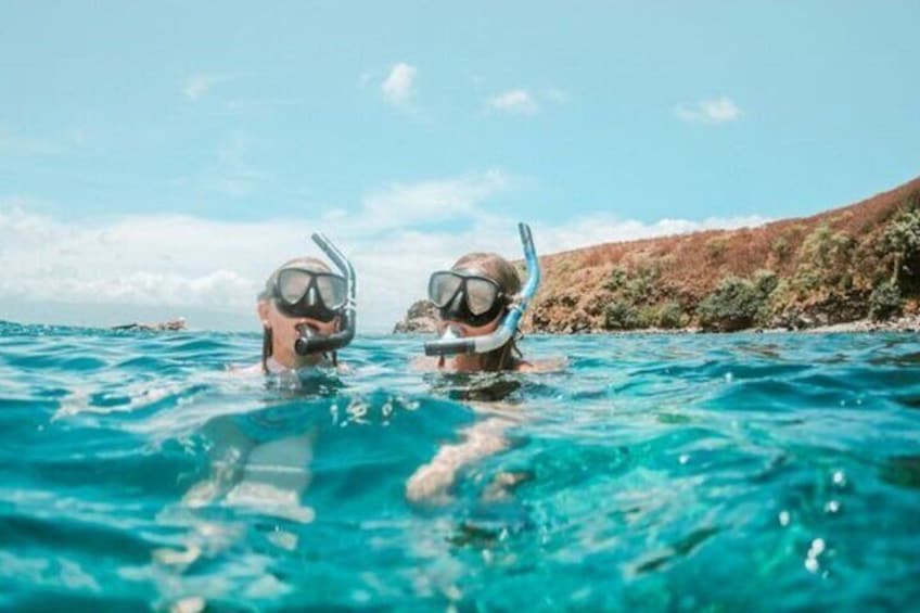 Two people snorkeling in clear blue water with a rocky coastline in the background. 5