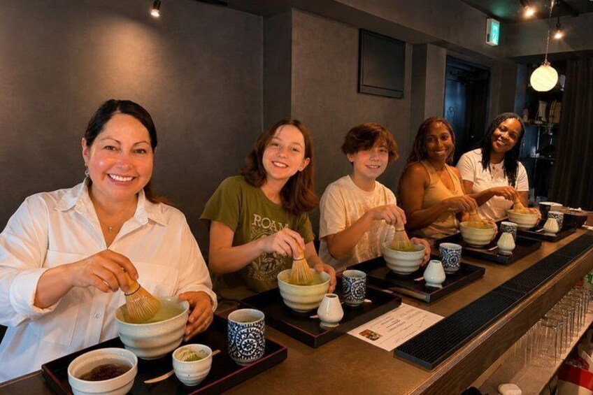 A group of people sitting at a counter, each with a bowl and chopsticks, likely participating in a dining activity. 1