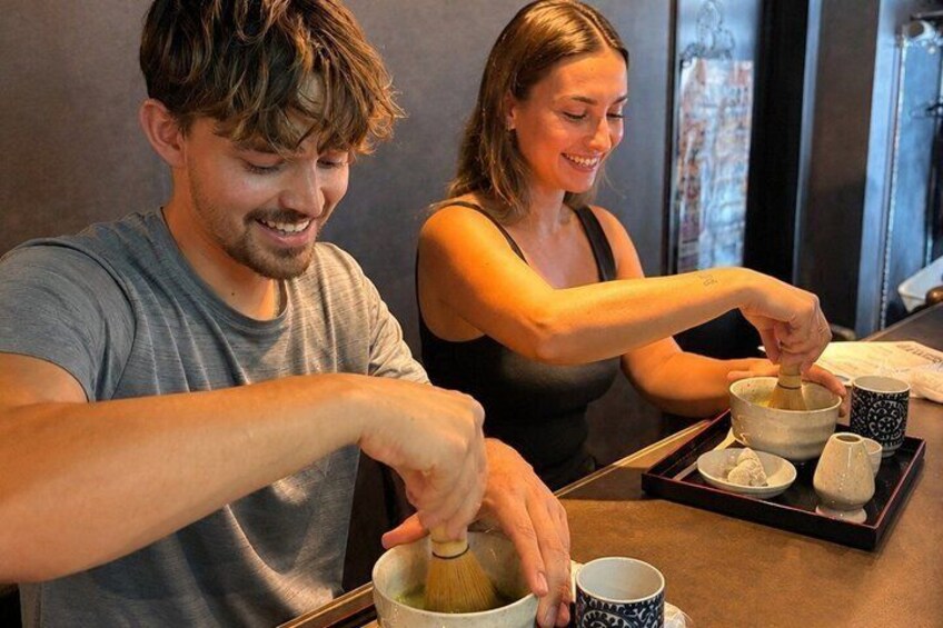 Two people preparing a drink with a whisk and a cup. 1