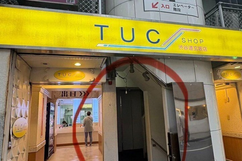 A TUC store entrance with a yellow sign, a person standing inside, and a red circular mark on the glass. 5