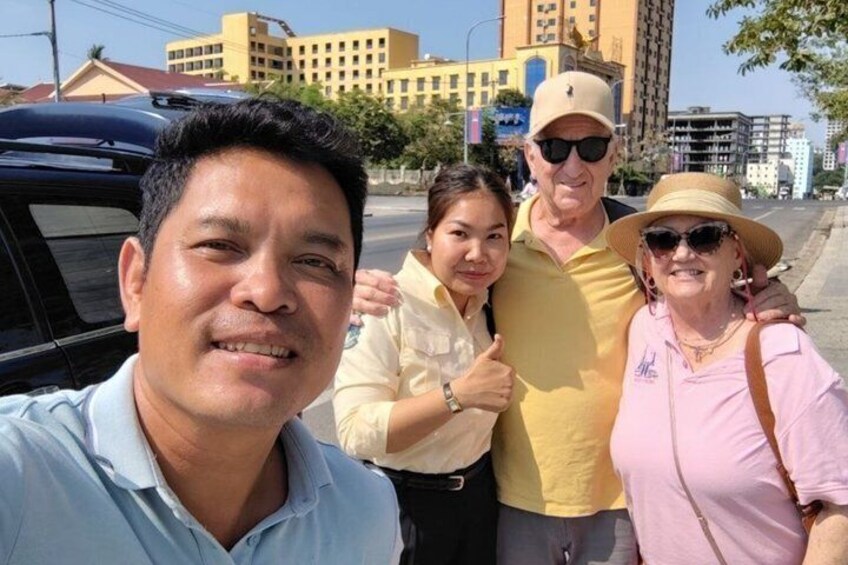 A group of people posing in front of a building with a yellow facade and a black car parked nearby. 1
