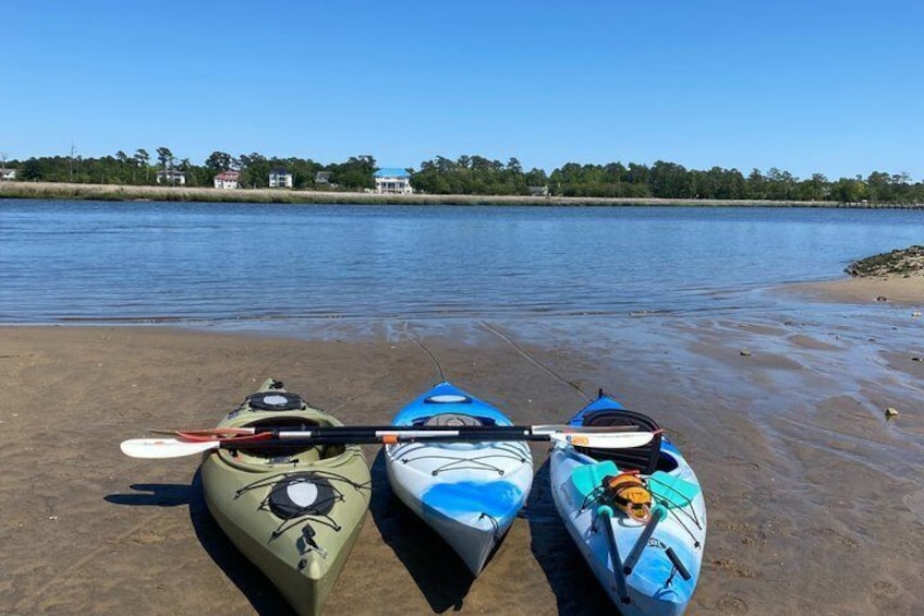 Three kayaks on a sandy beach with calm water and a clear sky. 1