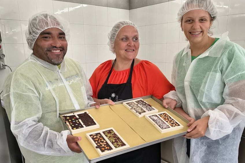 Three people wearing hairnets and aprons, holding a tray with various food items. 2