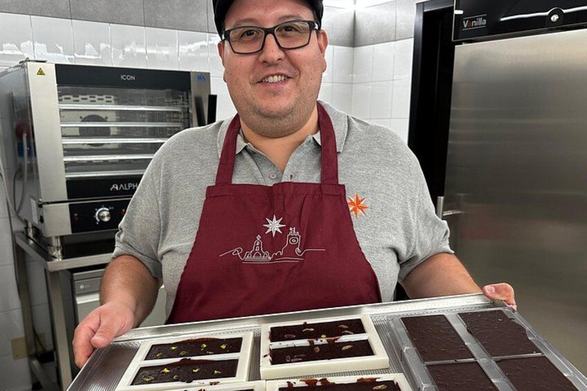 A person in a kitchen holding a tray with multiple chocolate desserts. 4