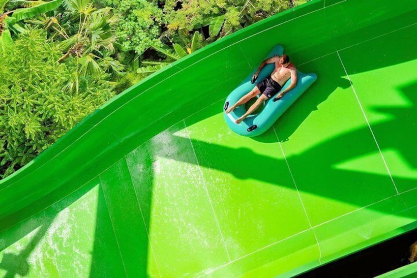 Una persona recostada sobre un flotador azul en un tobogán acuático verde brillante. 4