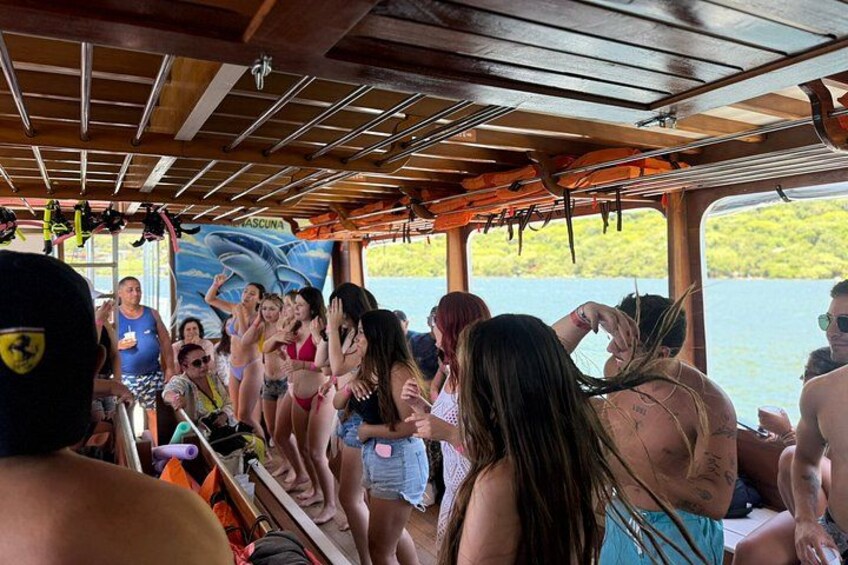 A group of people on a boat with a banner reading 'ASCUNDA' and a scenic view of a lake. 3