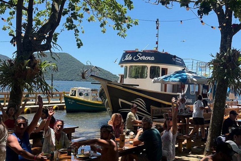 A boat named 'Isla Serena' docked at a waterfront restaurant with people dining and enjoying the view. 2