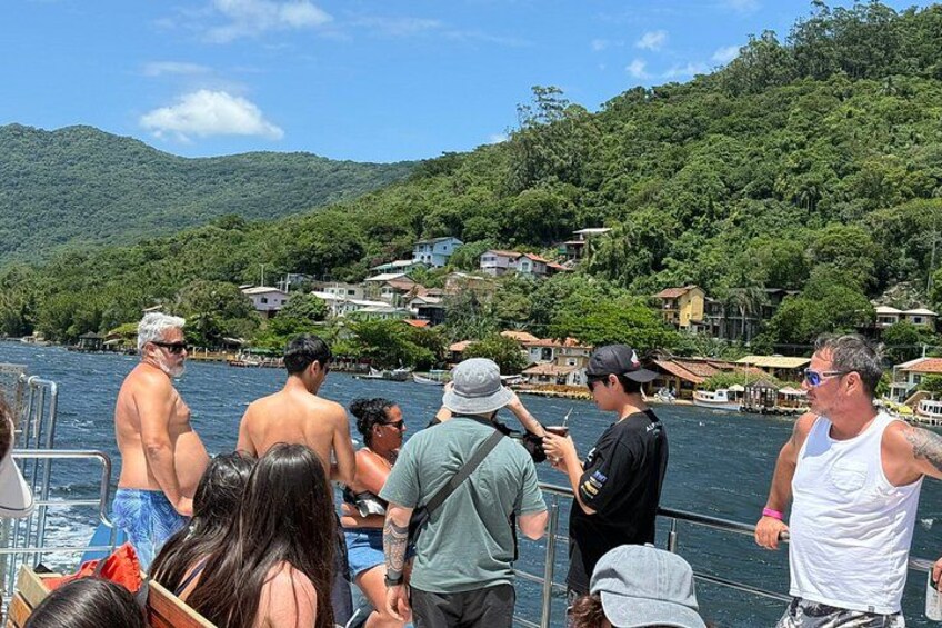 A group of people on a boat near a coastal village with houses and hills in the background. 3
