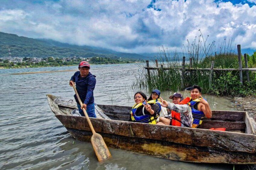 A group of people in a wooden boat on a calm river, with a person rowing and others sitting. 1