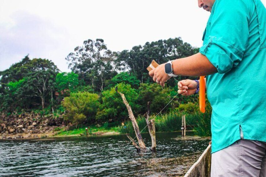 A person fishing by a calm river with trees and rocks in the background. 4
