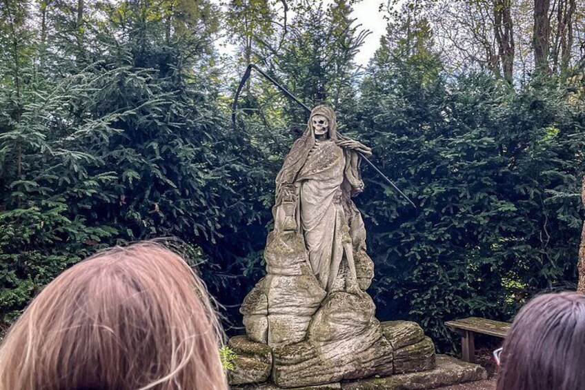 A stone statue of a figure with a spear, surrounded by dense forest. 4