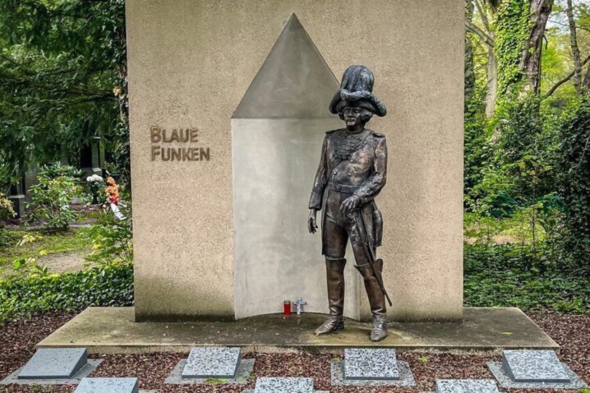 A statue of a historical figure with a label 'BLAUE FUNKEN' on a concrete base surrounded by greenery. 3