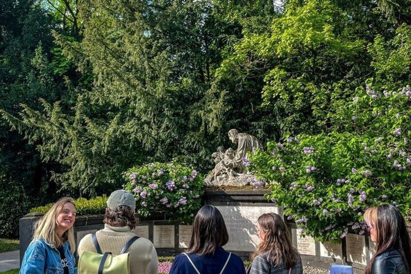 A group of people standing in front of a statue in a park with trees and flowers. 5