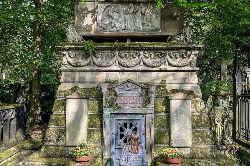 A stone monument with a carved figure, a door, and two flower pots. 1
