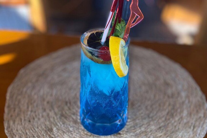 A blue beverage in a glass with a lemon slice and a red straw. 2