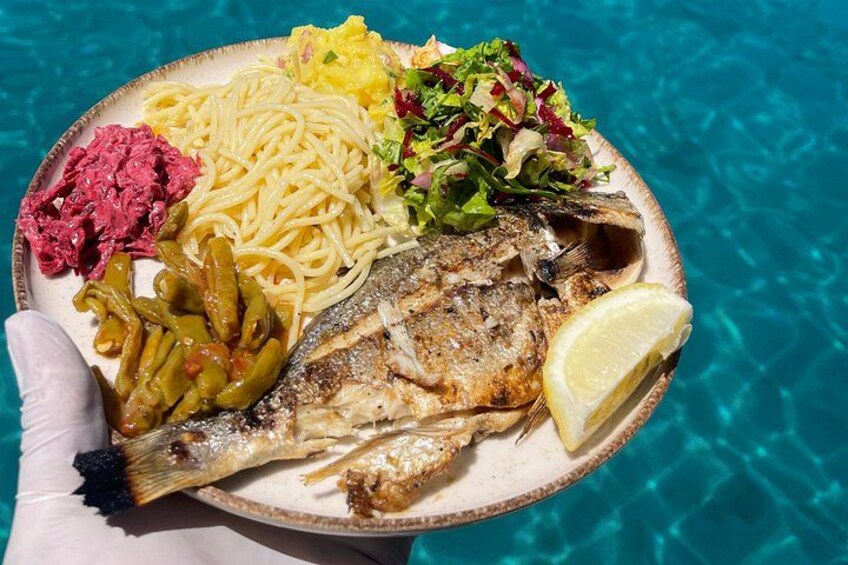 A plate of food with a fish, pasta, salad, and a lemon wedge. 3