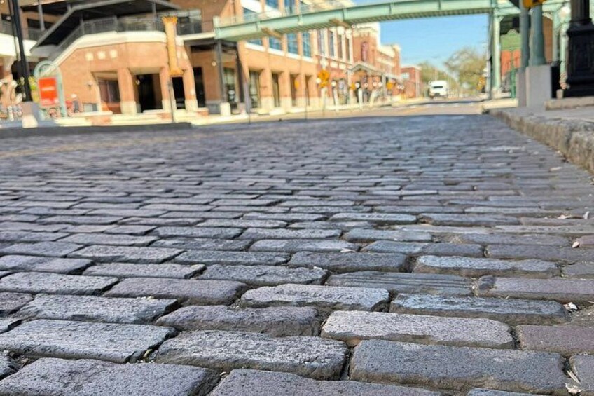 A cobblestone street with buildings and a bridge in the background. 2