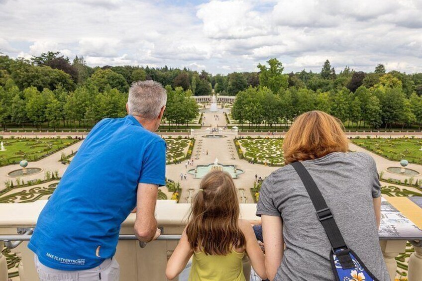 A family of three overlooking a formal garden with a central fountain and symmetrical landscaping. 4