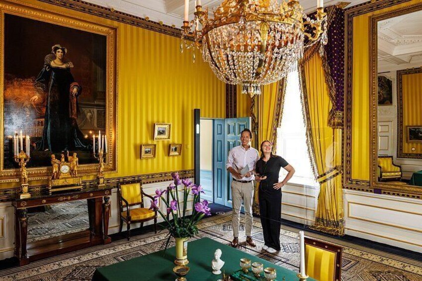 A grand room with a large chandelier, a portrait, and a table with flowers. 3
