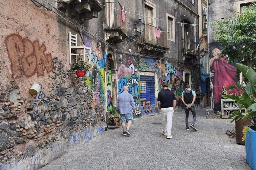 A narrow alley with graffiti, potted plants, and a mural on the wall. 3
