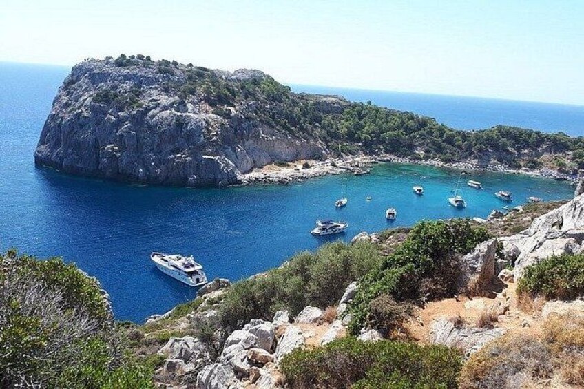 A rocky coastline with boats anchored in a bay. 4
