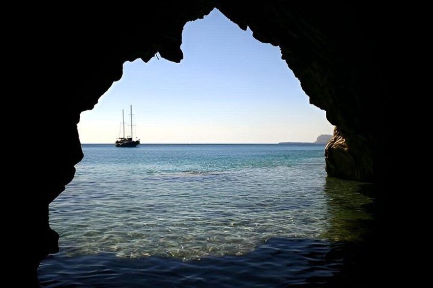 A sailboat on calm water, viewed through a cave opening. 2