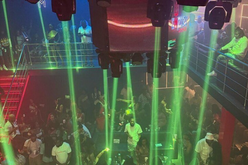 A crowded nightclub with green laser lights and a DJ booth. 1