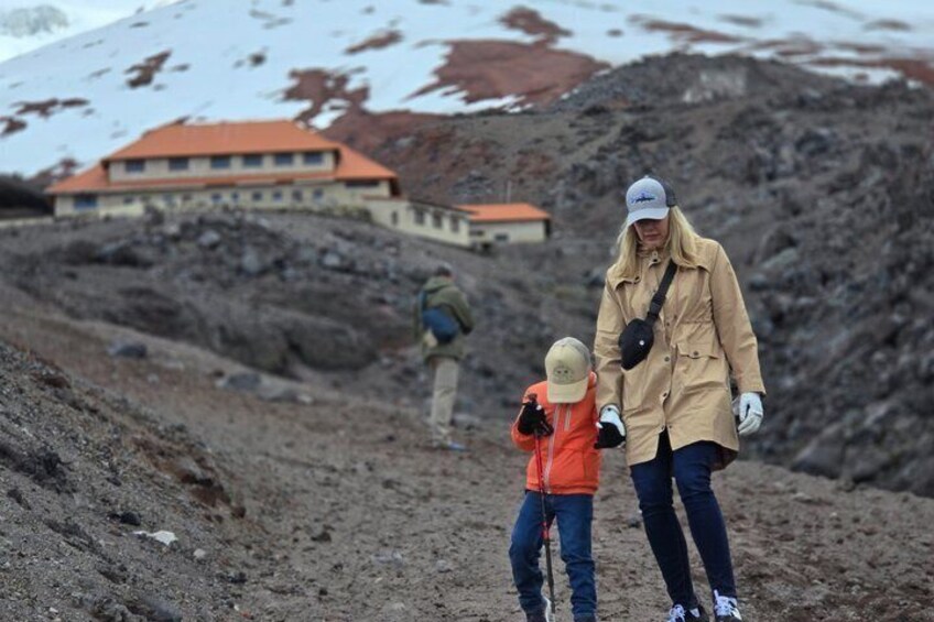 A person in a beige coat and a child in an orange jacket walking on a rocky slope with a building in the background. 4