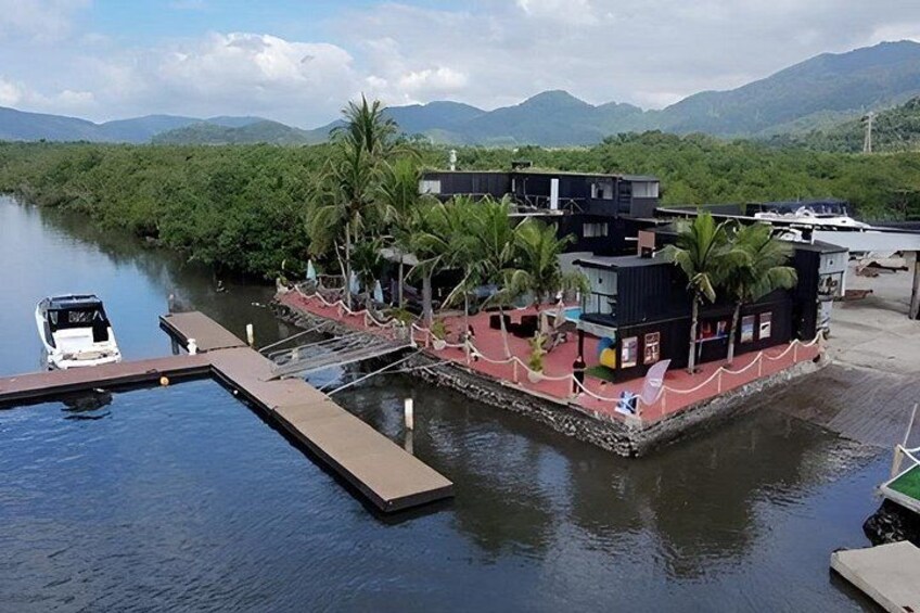 A dock with a boat, a floating structure with buildings, palm trees, and mountains in the background. 5