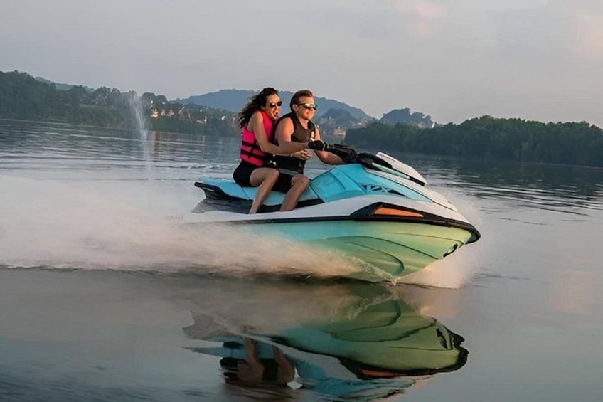Two people jet skiing on a calm lake with mountains in the background. 1