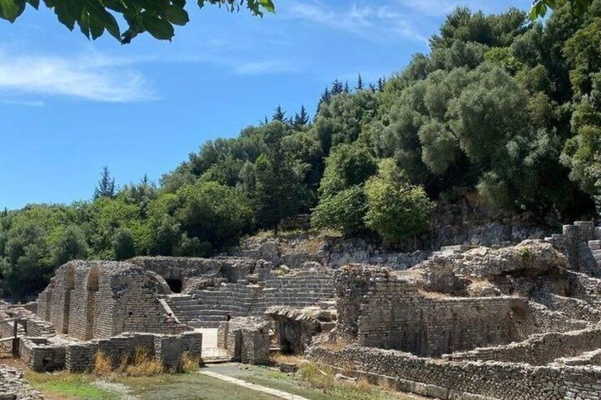 Ancient ruins with stone structures and a forested hillside in the background. 3