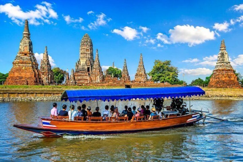 A boat with passengers and a blue canopy, navigating near ancient temple ruins by a river. 1