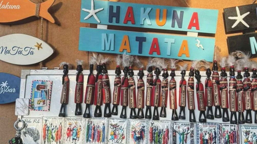 A display of traditional African attire and accessories, including beaded necklaces and headpieces, with a sign reading 'HAKUNA MATATA'. 1