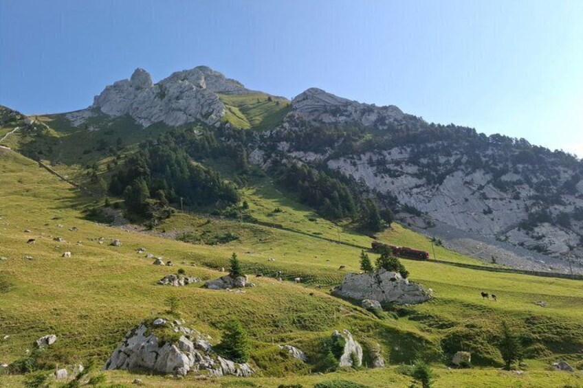 A mountainous landscape with green fields, scattered rocks, and a prominent rocky peak. 2
