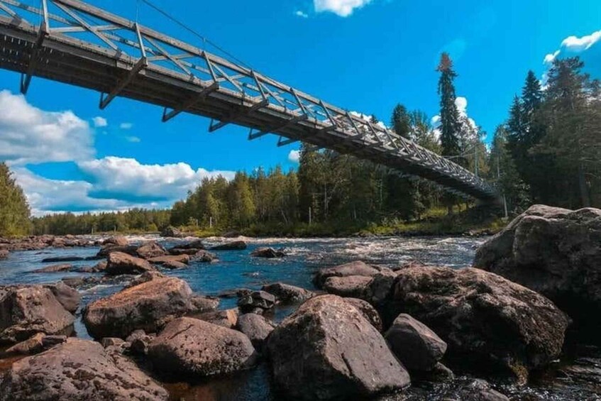A bridge over a river with large rocks in the foreground and trees in the background. 3
