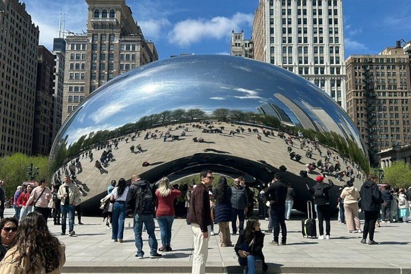 A large reflective sculpture surrounded by people in an urban setting. 1