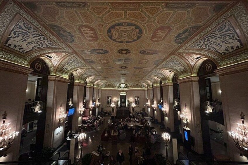 A grand hall with ornate ceiling artwork, chandeliers, and columns. 4