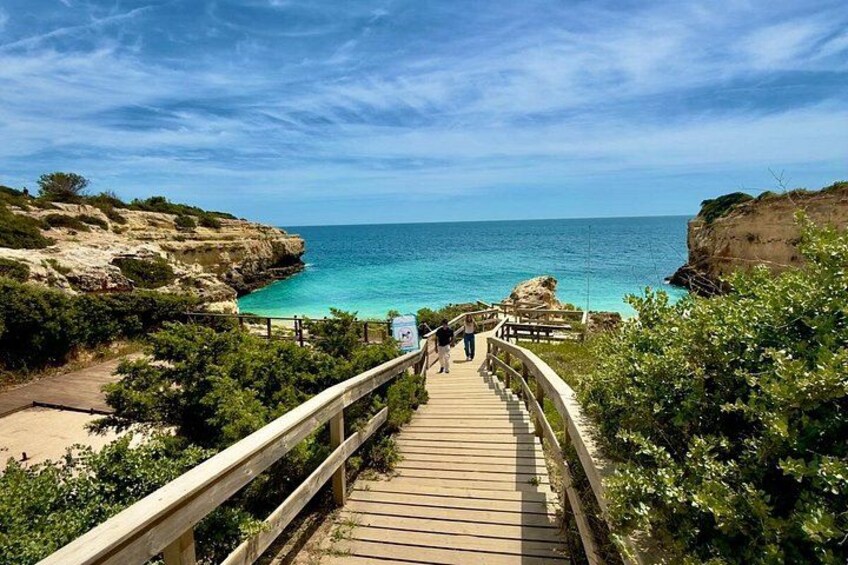 A wooden boardwalk leading to a beach with clear turquoise waters and rocky cliffs. 3
