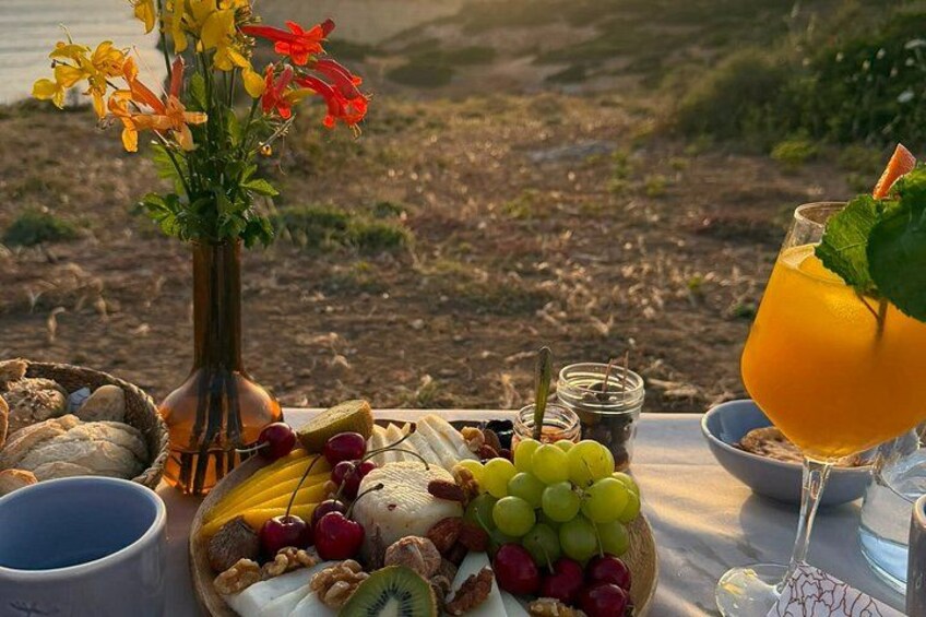 A picnic setup with a variety of fruits, nuts, and a drink on a table with a scenic view in the background. 2