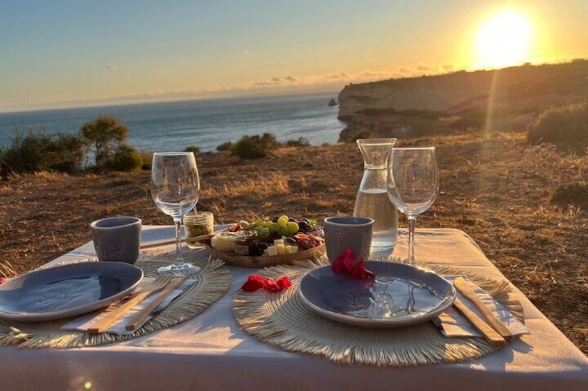 A table set for a meal with a view of the ocean and cliffs at sunset. 3