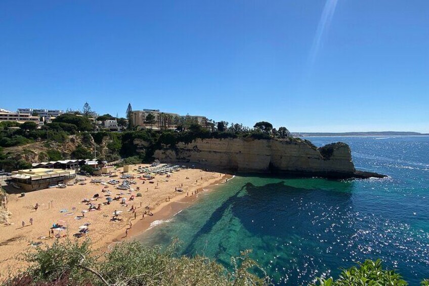 A coastal beach with clear water, a rocky cliff, and buildings in the background. 4