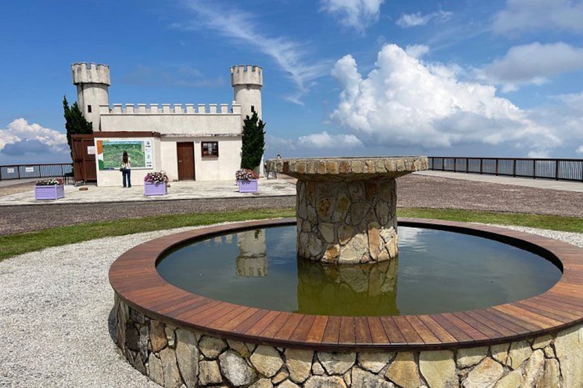 A castle-like structure with two towers, a stone fountain, and a wooden deck. 5