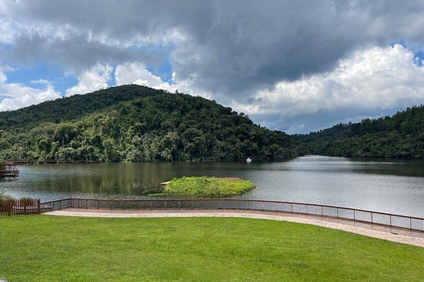 A lake surrounded by lush green hills, a wooden dock, and a paved walkway. 2