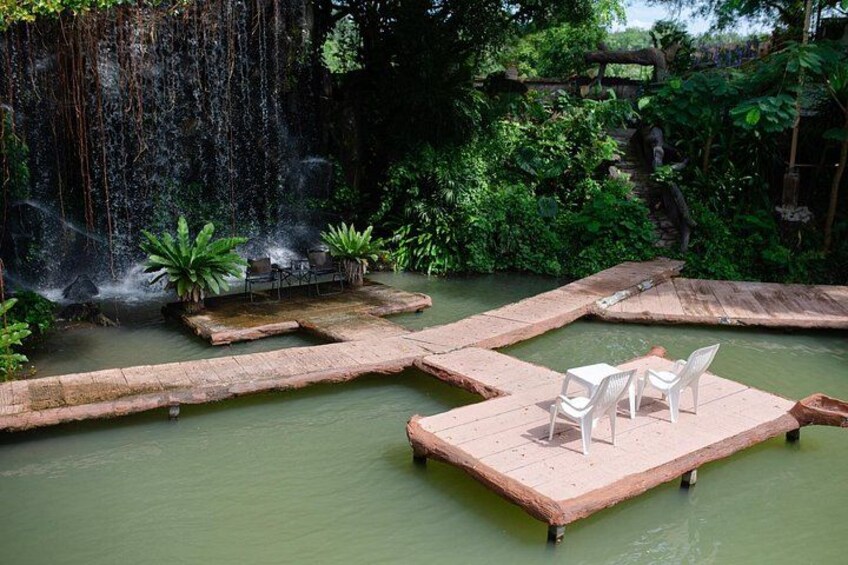 A serene water garden with a waterfall, floating platforms, and lush greenery. 4
