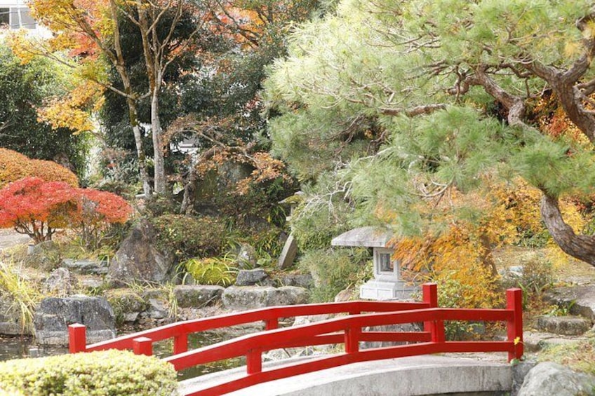 A red bridge over a pond with autumn foliage and a stone lantern. 2