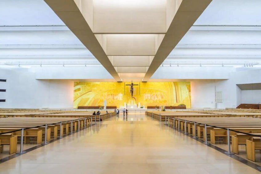 A church interior with rows of pews, a central altar, and a large stained glass window. 5