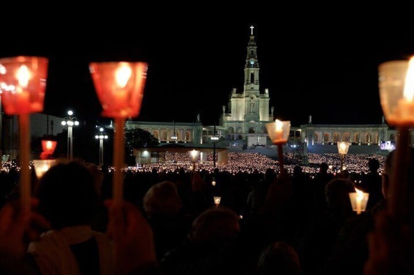 A crowd holding candles in front of a large building with a clock tower. 3