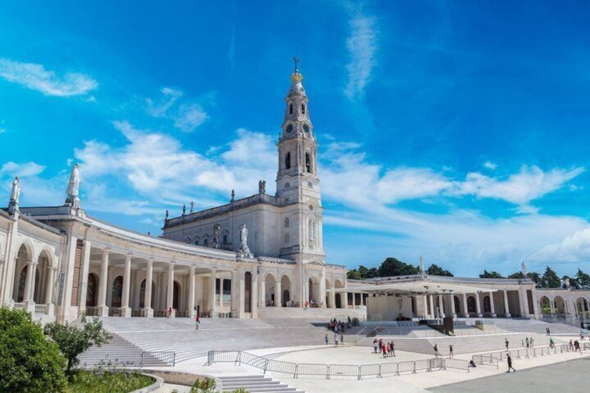 A large historical building with a prominent tower, a wide open plaza, and a clear blue sky. 1